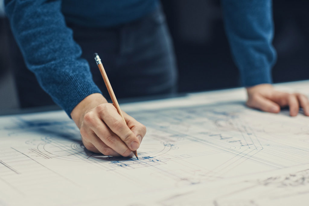 man in blue sweater working on blueprint with pencil